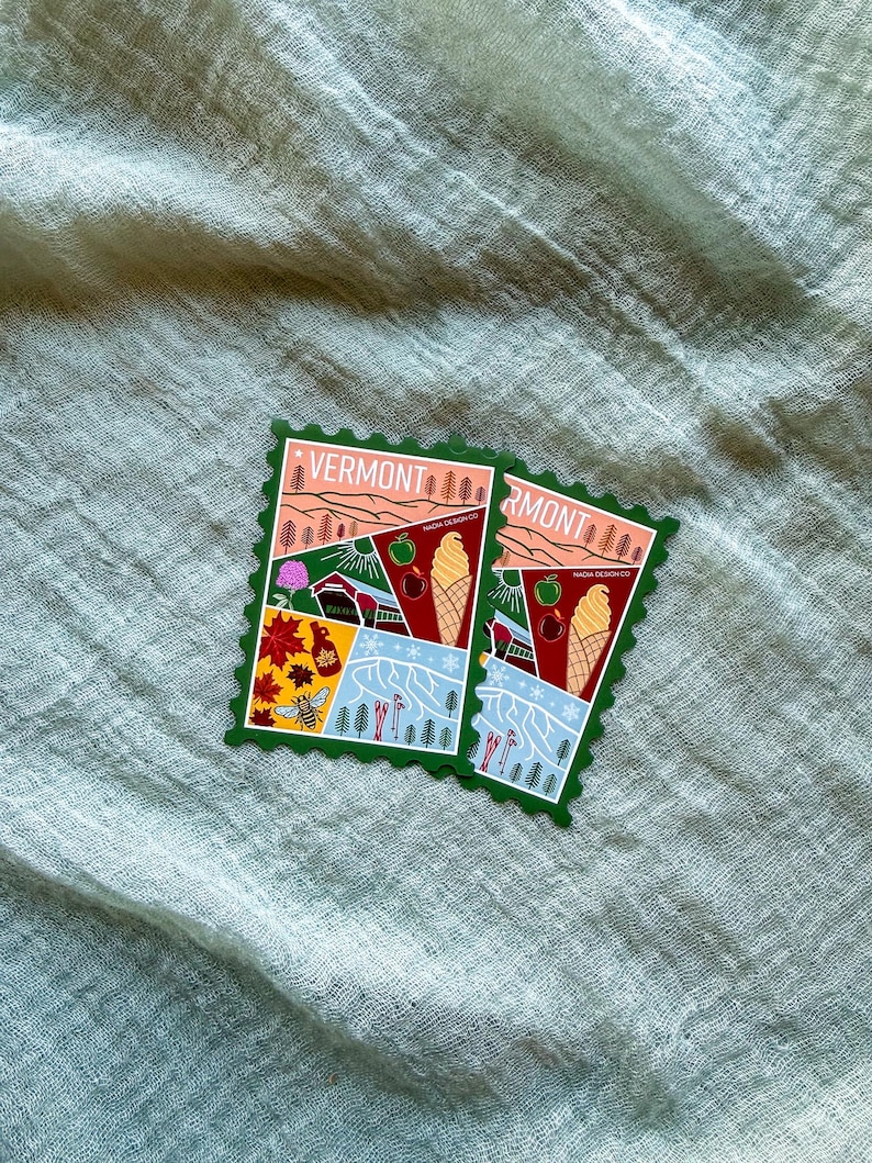 May include: Two Vermont-themed stickers with a postage stamp design. Each sticker features illustrations of a landscape with trees, a farm, ice cream cones, and the word "VERMONT". The stickers have a green border and are set against a light green fabric.