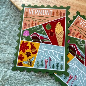 May include: A green-edged sticker with a Vermont theme, featuring illustrations of a red barn, apples, an ice cream cone, maple syrup, a bee, and skiers. The word "VERMONT" is at the top.