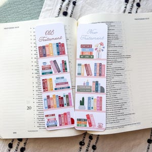 May include: Two decorative bookmarks with a bookshelf design are placed in an open book. One bookmark reads "Old Testament" and the other reads "New Testament." The bookmarks feature colourful book spines and small illustrations.