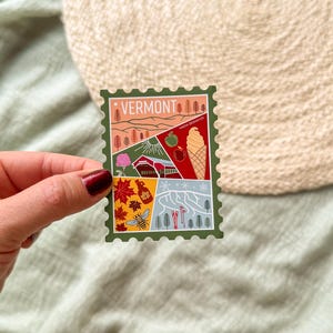 May include: A colorful sticker with a Vermont theme. The sticker features illustrations of a mountain landscape, an apple, an ice cream cone, and other Vermont icons. The word "VERMONT" is printed at the top.