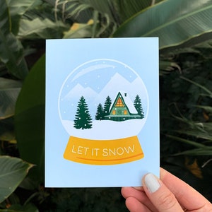 Laissez-le neiger carte de Noël | Taille 5,5 x 4,25 po. avec enveloppes | Cadeaux d'illustration de cabane d'hiver dans les montagnes de boules à neige dans les bois