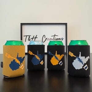 May include: Four beverage can coolers with a West Virginia state outline design. The coolers are in mustard yellow and black, with blue, yellow, and gray graphics. The text "T&H Creations" is in a black frame in the background.