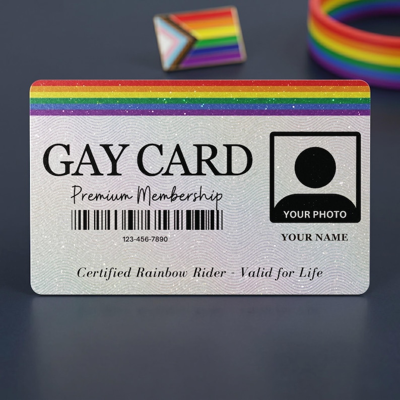 Front view of a custom 'GAY CARD Premium Membership' featuring a rainbow stripe, a glittery background, barcode, 'YOUR PHOTO' placeholder, and 'YOUR NAME' placeholder. 'Certified Rainbow Rider - Valid for Life' is printed below. A pride pin and rainbow bracelet are in the background.