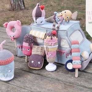 Könnte beinhalten: Ein gehäkelter Eiswagen mit verschiedenen gehäkelten Eisbeilagen, darunter ein Donut, ein Eis am Stiel, eine Eistüte und ein Milchshake. Der Wagen ist blau und weiß mit einem gestreiften Vordach. Die Eisbeilagen sind alle bunt und haben süße Gesichter.