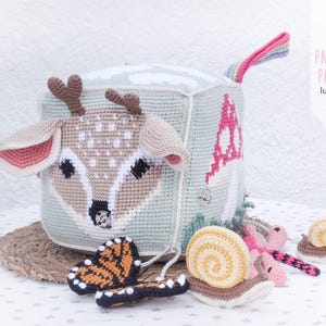 May include: A handmade crochet cube toy featuring a deer face, a mushroom, and a rainbow handle. The cube is light blue and beige, with brown antlers and pink accents. Includes a crochet butterfly and snails.