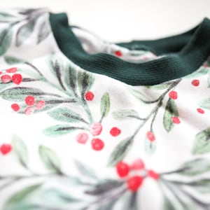 May include: White long-sleeved shirt with a green ribbed neckline and a green and red holly berry print.