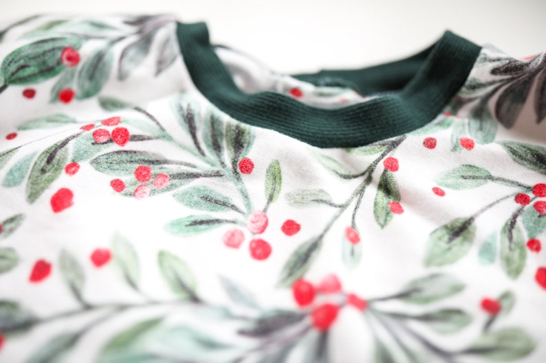 May include: White long-sleeved shirt with a green ribbed neckline and a green and red holly berry print.