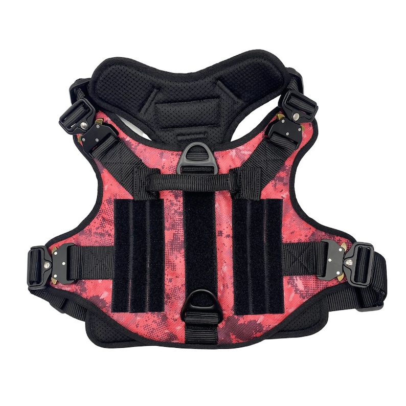 May include: A red and black dog harness with adjustable straps and a padded chest piece. The harness has a camouflage pattern and multiple D-rings for leash attachment.