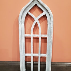 May include: White painted wooden arched window frame with a decorative grid pattern. The frame is a wall decor piece.