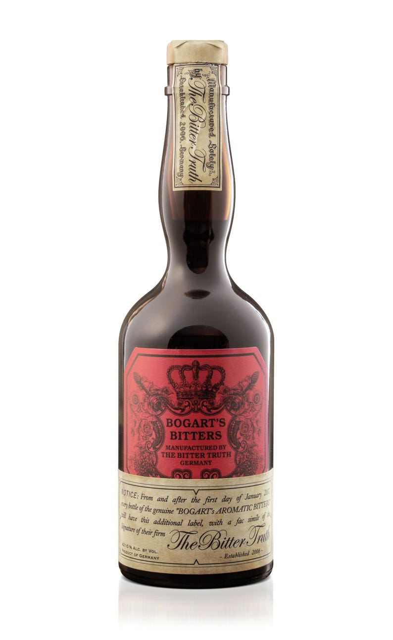 May include: A dark glass bottle of Bogart's Bitters, with a red label featuring a crown and ornate text. The label reads "Manufactured by The Bitter Truth Germany." The bottle has a paper seal.