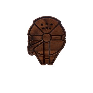 May include: A wooden wall decor in the shape of the Millennium Falcon spaceship from Star Wars. The decor is brown and has a detailed carving of the spaceship.