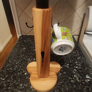May include: Wooden mug rack with a clover-shaped base and three hooks. A green and white mug with a cartoon design is hanging on one of the hooks.