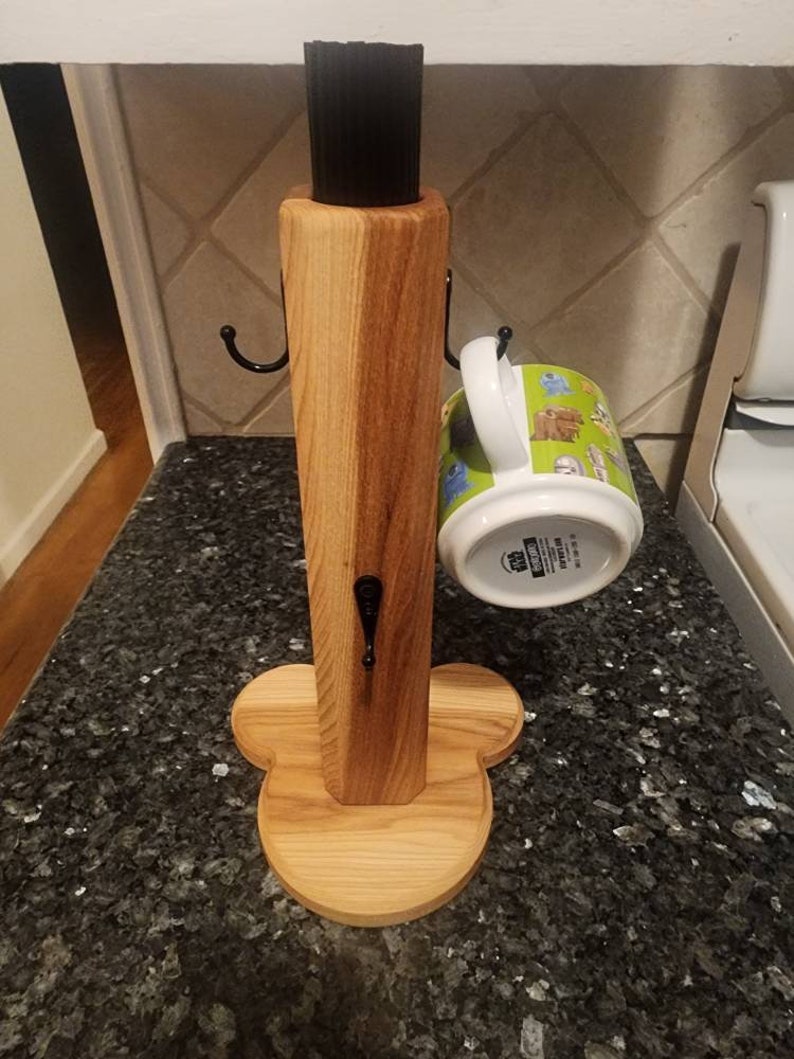 May include: Wooden mug rack with a clover-shaped base and three hooks. A green and white mug with a cartoon design is hanging on one of the hooks.