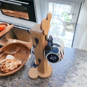 May include: Wooden mug holder shaped like Mickey Mouse with four hooks and a black mug hanging from one of the hooks.