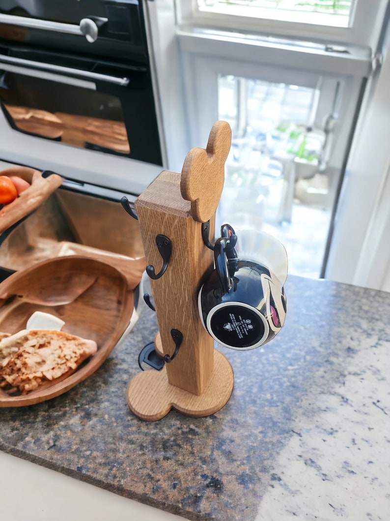 May include: Wooden mug holder shaped like Mickey Mouse with four hooks and a black mug hanging from one of the hooks.