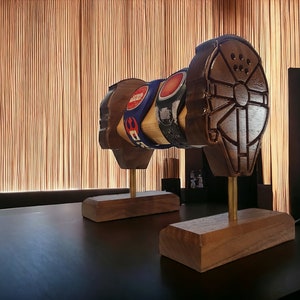 May include: Two wooden Star Wars themed bottle stoppers on wooden bases. The stoppers are shaped like the Millennium Falcon and the Death Star.