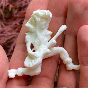 Könnte beinhalten: Weiße Plastikfigur einer Person, die Gitarre spielt. Die Figur ist in einer dynamischen Pose mit einem erhobenen Bein und der Gitarre, die vor dem Körper gehalten wird.