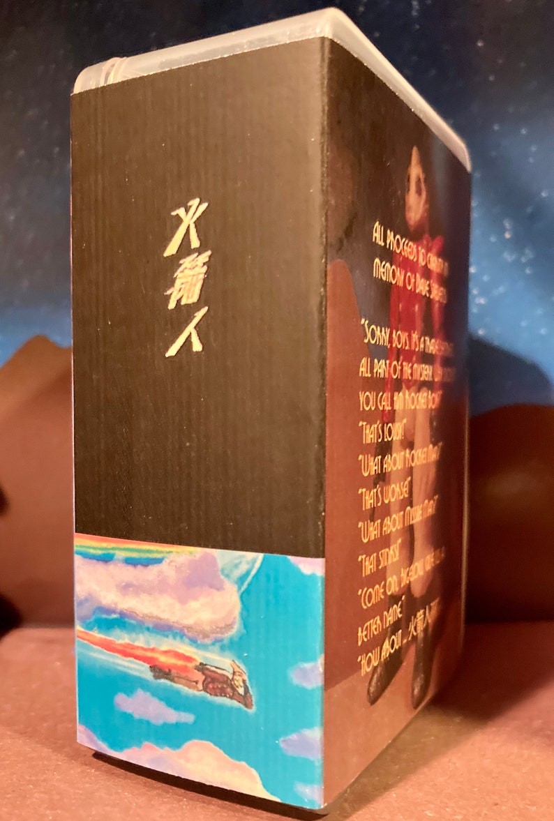 May include: A VHS tape with a black background and a rainbow and blue sky with a flying figure. The text on the tape reads "ALL PROCEEDS TO CREATE A MEMORY OF DAVE STREET" and "SORRY, BOYS, IT'S A TRAGEDY. ALL PART OF THE NORTHERN LIGHTS. YOU CALL HIM NONE OTHER THAN... THAT'S LOW. WHAT ABOUT ROCKET MAN? THAT'S WORSE. WHAT ABOUT MIKE THAT? THAT STINKS. COME ON, BACK ON THE... BETTER NAME. HOW ABOUT..."