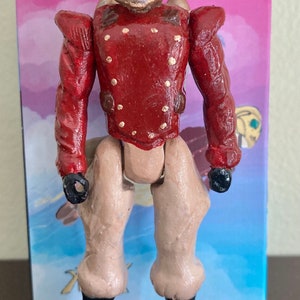 May include: A hand-painted action figure with a gold and brown helmet, a red jacket with gold buttons, and tan pants. The figure is wearing black boots.