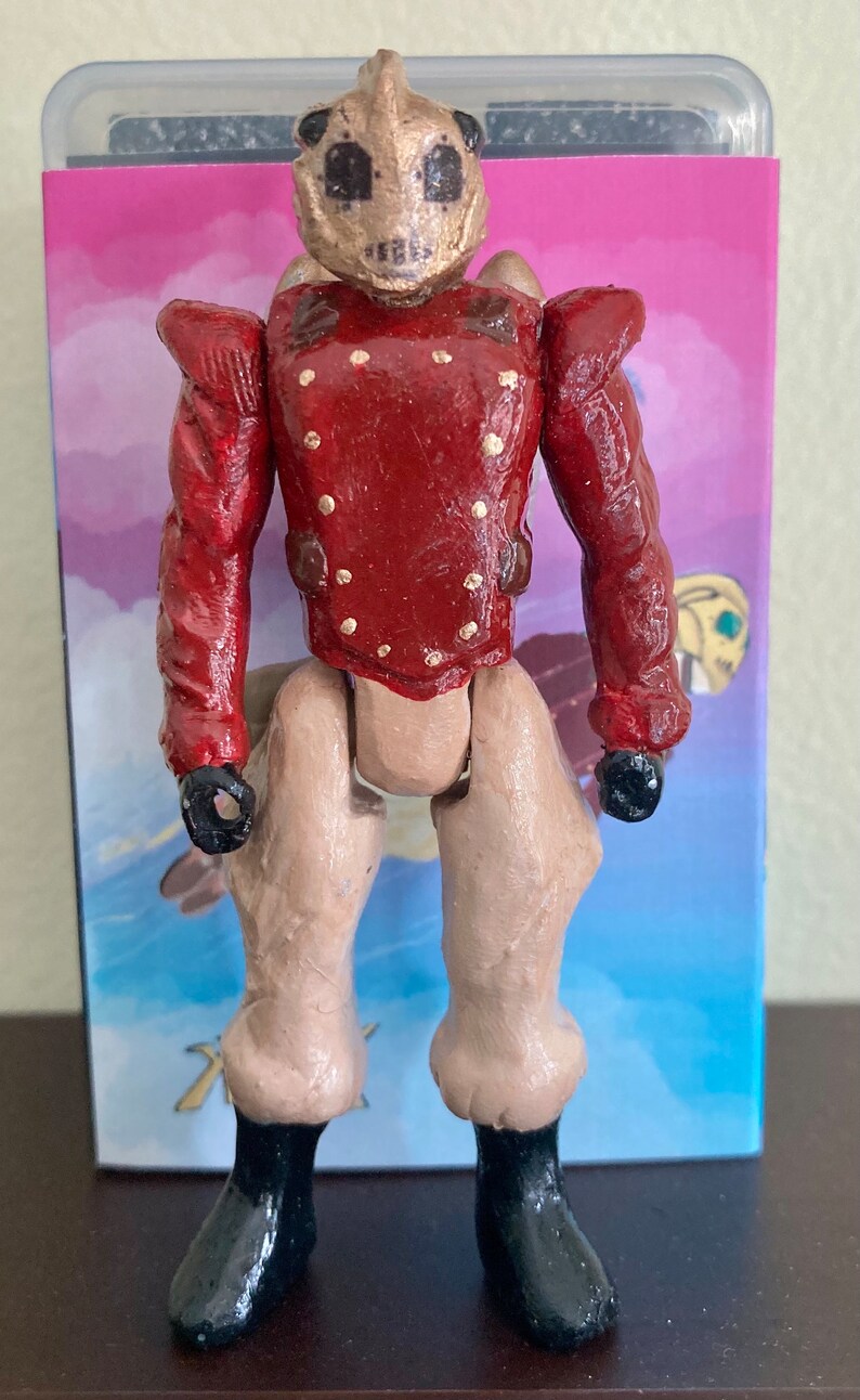 May include: A hand-painted action figure with a gold and brown helmet, a red jacket with gold buttons, and tan pants. The figure is wearing black boots.