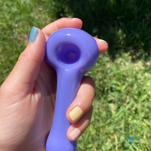 May include: A purple glass pipe with a rounded bowl and a long, slender stem.