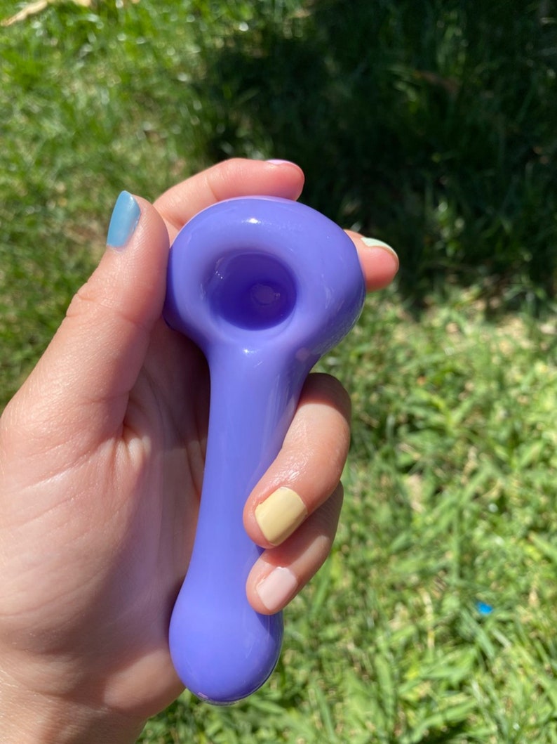 May include: A purple glass pipe with a rounded bowl and a long, slender stem.