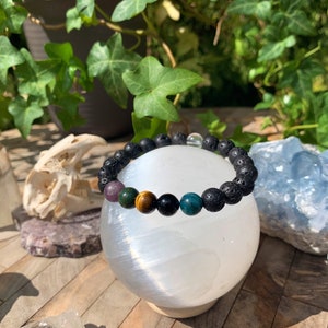 Op de afbeelding: Een zwarte lava armband met verschillende edelsteen kralen, waaronder amethist, tijgeroog, zwarte onyx en groene aventurijn.