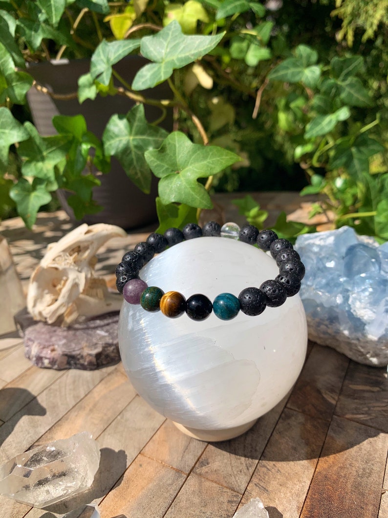 Op de afbeelding: Een zwarte lava armband met verschillende edelsteen kralen, waaronder amethist, tijgeroog, zwarte onyx en groene aventurijn.