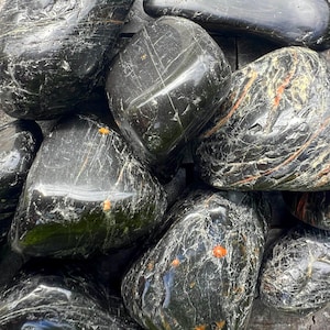 May include: A collection of smooth, black and grey polished stones with white and orange veins. The stones are various sizes and shapes.