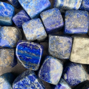 May include: A collection of tumbled lapis lazuli stones. The stones are a deep blue color with flecks of gold pyrite. The stones are smooth and polished.