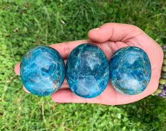 May include: Three smooth, polished blue apatite palm stones. The stones are a deep blue with a marbled pattern and a glossy finish.