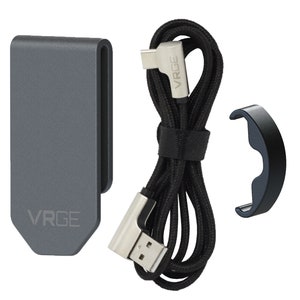 Puede incluir: Un clip de metal gris con la palabra "VRGE" en él, un cable trenzado negro con un conector USB-C en ángulo recto en un extremo y un conector USB-A en el otro extremo, y un clip de cable de plástico negro.