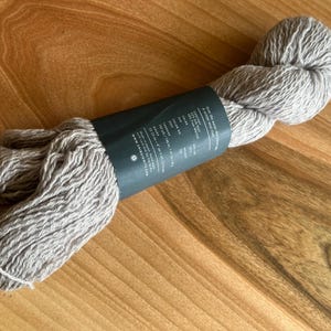May include: A skein of light gray yarn with a black and white label that reads "Our fingering weight yarn is a smooth and soft merino wool."