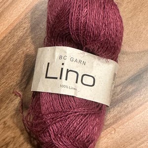 May include: A ball of deep red linen yarn with a label that reads "BC Garn Lino 100% Linen".
