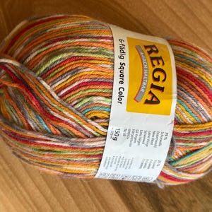 May include: A ball of Regia 6-fädig Square Color yarn. The yarn is a mix of colors including red, orange, yellow, green, and white. The label indicates the yarn is 150g.