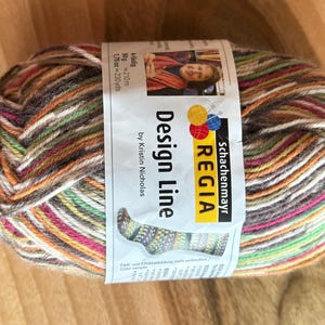 May include: A ball of multi-coloured yarn with a label that reads "Schachenmayr REGIA Design Line by Kristin Nicholas". The yarn is a mix of brown, white, orange, red, green, and yellow.