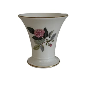 May include: A white ceramic vase with a gold rim and a floral design featuring a pink rose and green leaves.