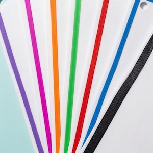May include: A set of rectangular white bookmarks arranged in a fan shape. Each bookmark features a distinct coloured border in purple, pink, orange, green, red, blue, or black. Every bookmark includes a small circular hole at the top corner.