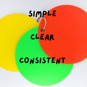 May include: Three overlapping, colourful, circular tags connected by a silver ring. The tags are yellow, green, and red. The words "SIMPLE", "CLEAR", and "CONSISTENT" are written in black on the tags. The bottom right corner has the logo "SEN Talk Tags".