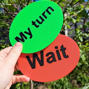 May include: Two oval-shaped signs with black text. The top sign is bright green with the text "My turn" in a bold sans-serif font. The bottom sign is bright orange-red with the text "Wait" in a bold sans-serif font. Both signs have a textured finish.