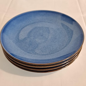 May include: A stack of four blue ceramic dinner plates with a brown rim.