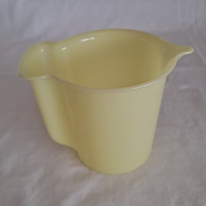 Puede incluir: Una jarra de plástico de color amarillo pálido con asa y pico. La jarra está vacía y tiene una superficie lisa.
