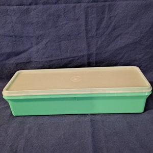 May include: A light green rectangular plastic storage container with a white lid. The lid has the words "Tupperware" printed on it.