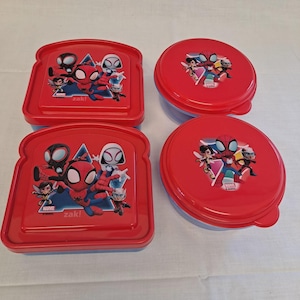 May include: Four red and blue plastic food containers. Two are rectangular, shaped like bread, and two are round. Each lid features a Marvel Spider-Man graphic with the text "zak!" and Marvel logos.