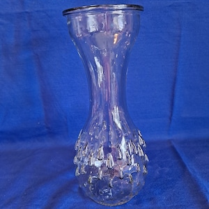 May include: A clear glass vase with a textured, bulbous base and a long, slender neck. The vase has a textured, bubbly surface.