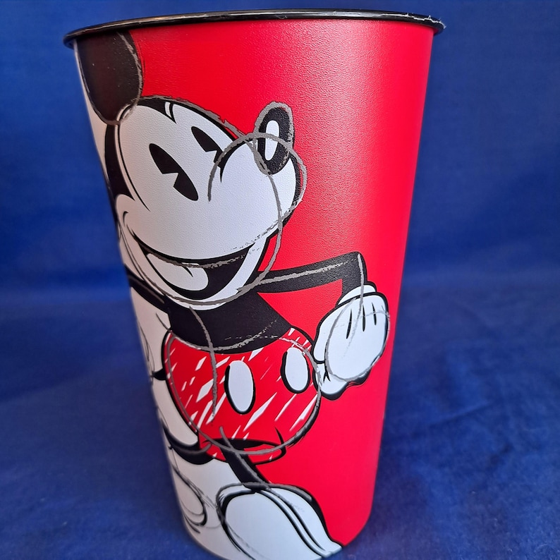 Puede incluir: Un vaso alto rojo con un borde negro, con un gr&aacute;fico de Mickey Mouse sonriente. El vaso tiene un fondo rojo vibrante. Mickey Mouse est&aacute; representado en su esquema de color cl&aacute;sico negro, blanco y rojo, con una expresi&oacute;n juguetona.