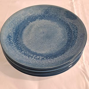 May include: A stack of five blue ceramic plates. The plates have a speckled, textured surface with a gradient of light to dark blue. The plates are round and have a slightly raised edge.