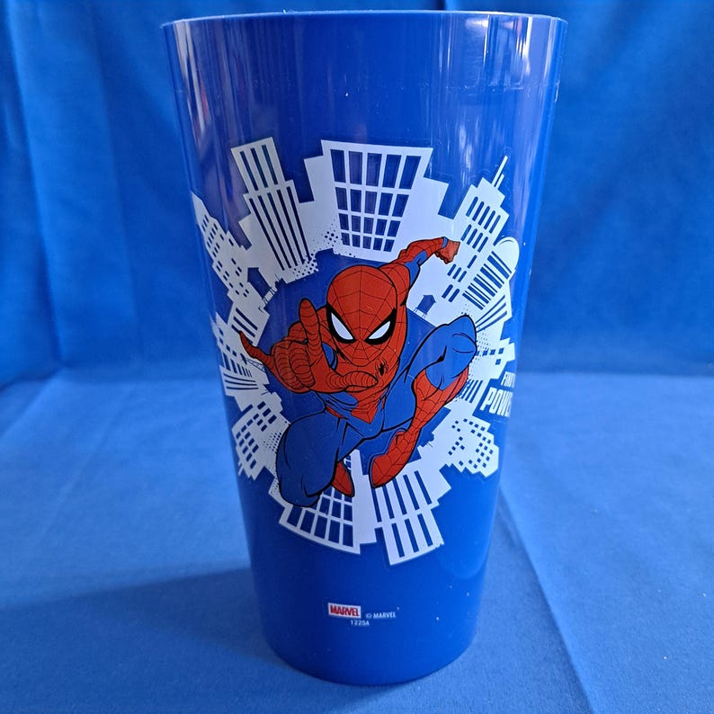 May include: A blue plastic cup featuring Spider-Man in a dynamic pose, set against a cityscape backdrop. The cup has the Marvel logo at the bottom. The cup is approximately 6 inches tall.