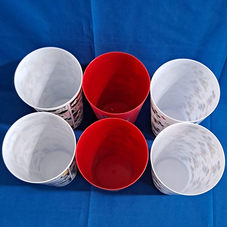 Puede incluir: Vista superior de seis vasos de pl&aacute;stico. Dos vasos rojos en el centro. Dos vasos blancos con un dise&ntilde;o en blanco y negro. Dos vasos blancos con un dise&ntilde;o moteado. Todos los vasos est&aacute;n sobre una superficie azul.