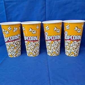 Peut inclure: Quatre gobelets à popcorn jaunes avec des couvercles blancs. Les gobelets ont un motif de popcorn noir et blanc et le mot "Popcorn" en lettres rouges.